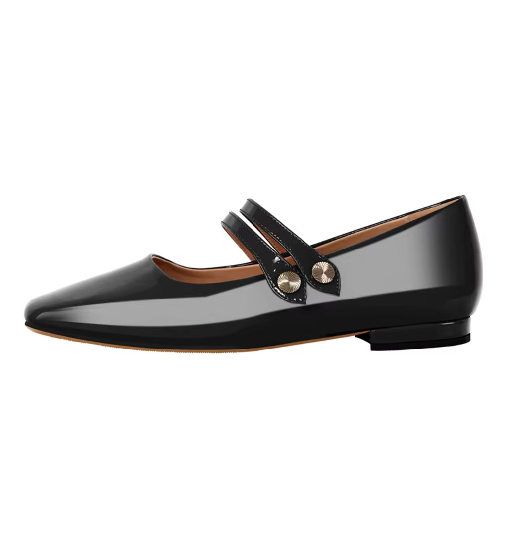 Black patent leather flat shoe with a strap and gold buckle on a white background