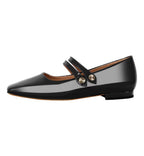 Black patent leather flat shoe with a strap and gold buckle on a white background