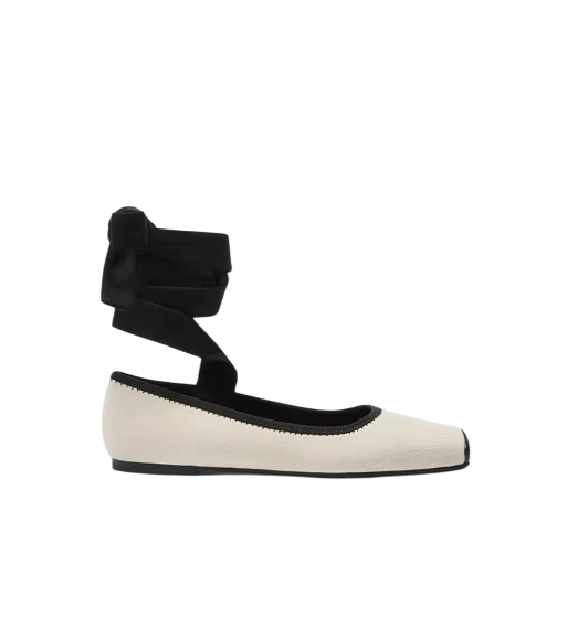 White flat shoe with black ankle strap on a white background