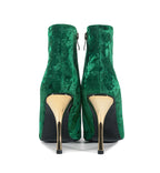 Green velvet high-heeled shoes with gold soles on a white background